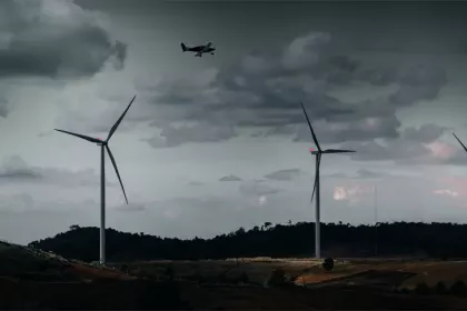 Ein mit BNK ausgestatteter Windpark mit mehreren Windturbinen und einem darüber fliegenden Flugzeug vor einem Hintergrund von dunklem, bewölktem Wetter.